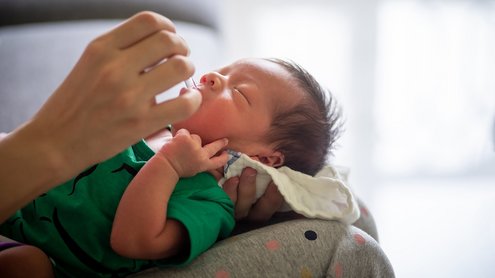 Säugling wird gehalten und Vitamintropfen in seinen Mund getröpfelt.