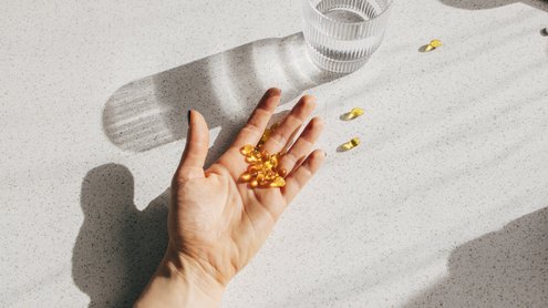 Eine Hand hält mehrere Vitamin-Tabletten. Ein Wasserglas steht daneben.