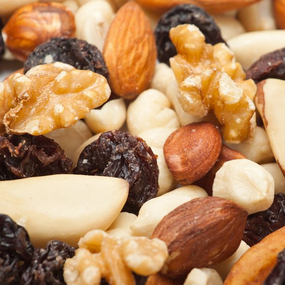 Verschiedene Nüsse (Walnüsse, Haselnüsse, Cashews Pecannüsse und Erdnüsse) sowie Rosinen liegen auf einem Tisch.